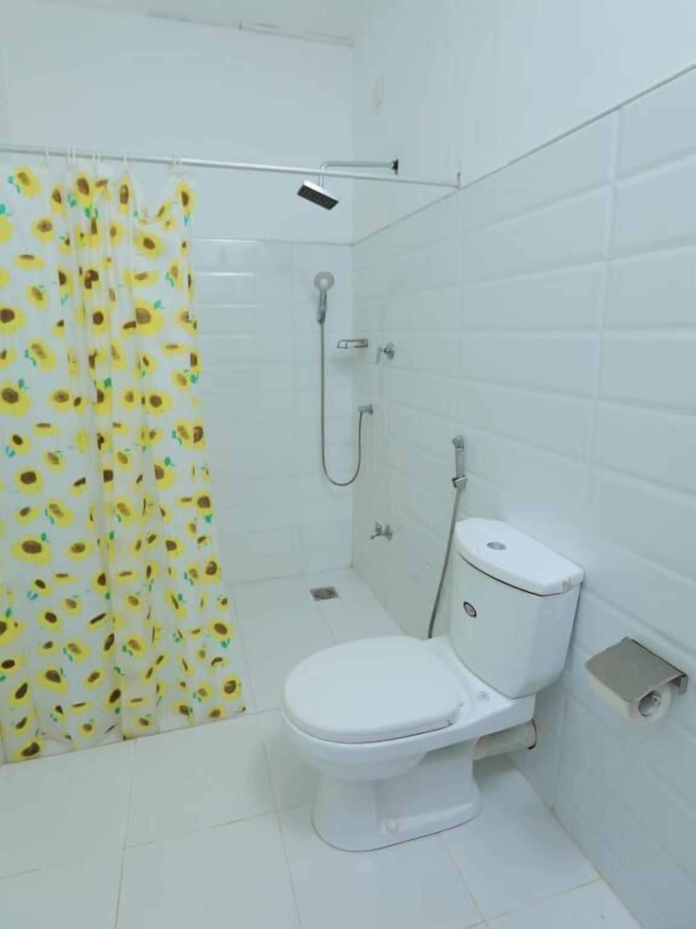 A small, white bathroom with a shower, toilet, and a curtain with a sunflower pattern.