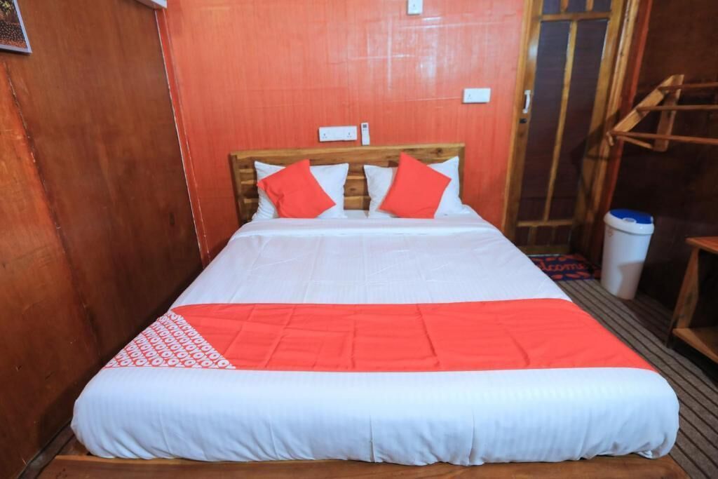 A single bed with a wooden headboard, white and red bedding, and a red throw blanket.