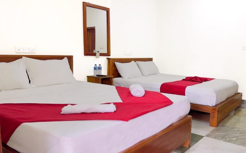 Two single beds with wooden frames, white and red bedding, a wooden nightstand with a remote control, and a mirror on the wall.