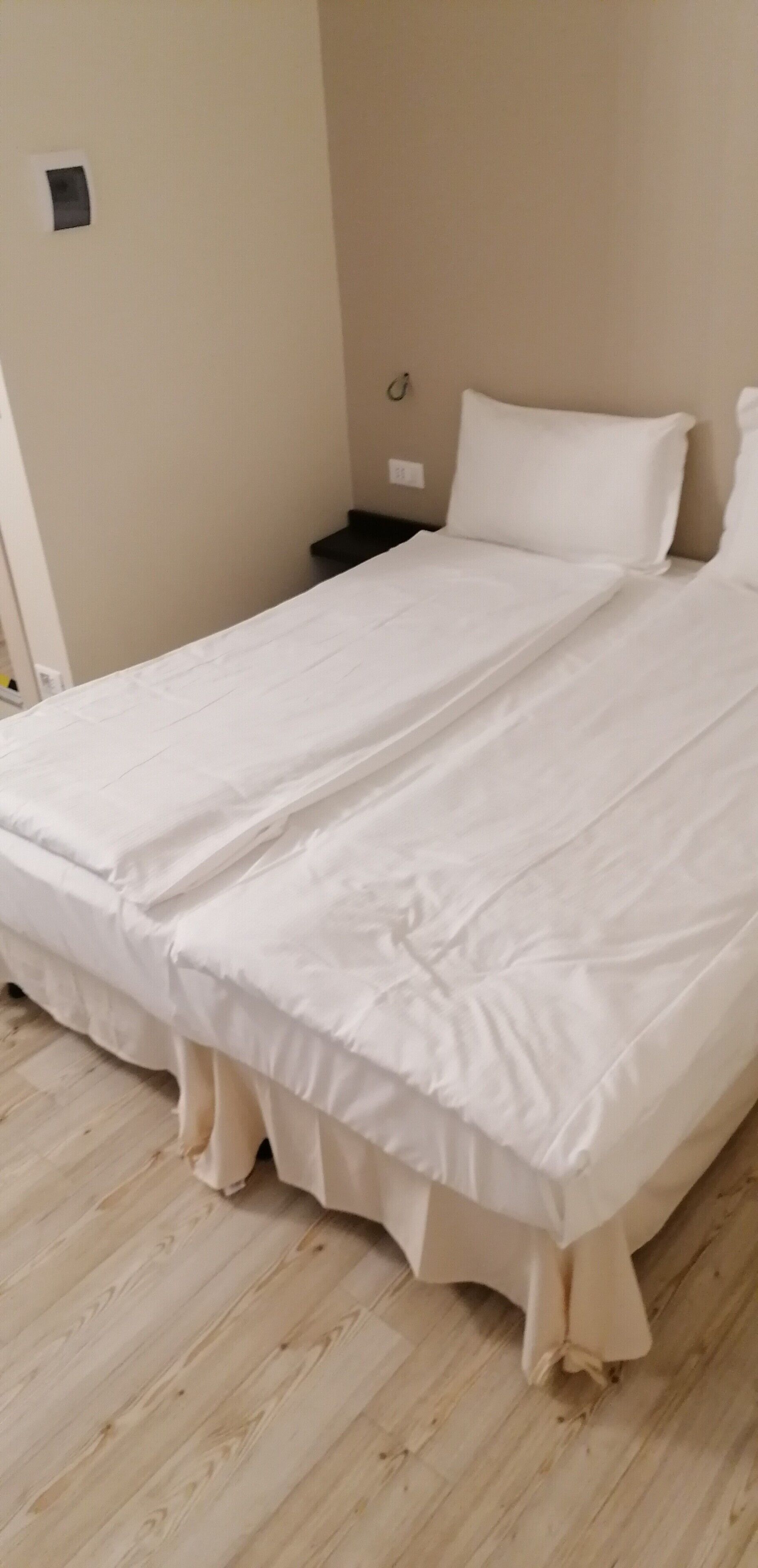 A single-bed room with a wooden floor, white bedding, and a small bedside table.