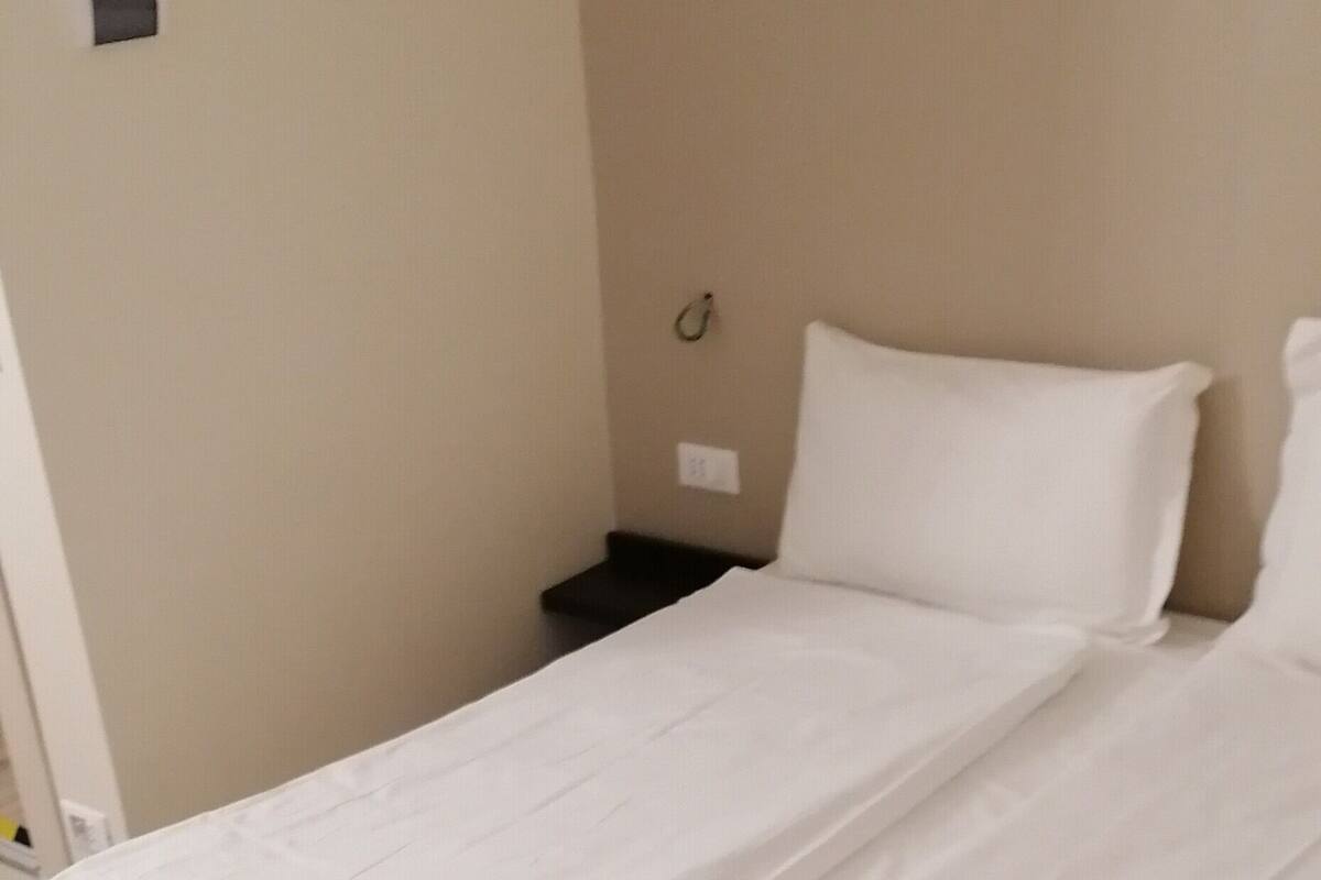 Ein Zimmer mit einem Einzelbett, Holzboden, weißer Bettwäsche und einem kleinen Nachttisch.