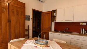 A compact kitchen with wooden cabinets, a dining table with a basket, and a view into the adjacent room. - Apartment for 4 in Quartu, near Poetto, Cagliari and nature, comfortable and complete (Quartu Sant'Elena)
