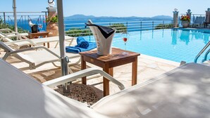 A poolside area with lounge chairs, a table with a bottle and glasses, and a view of the sea and mountains. - Villa Anthula mit Pool und herrlichem Meerblick by Interhome (Kalami)