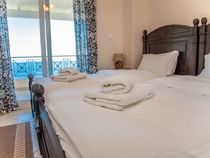 A hotel room with two beds, each with neatly folded white towels, a wooden headboard, and a view of the sea through large windows. - Villa Sotiris mit Pool und herrlichem Meerblick by Interhome (Kalami)