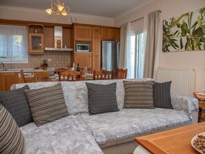 A cozy living room with a sofa, a dining table, and a kitchen area with wooden cabinets and a microwave. - Villa Sotiris mit Pool und herrlichem Meerblick by Interhome (Kalami)