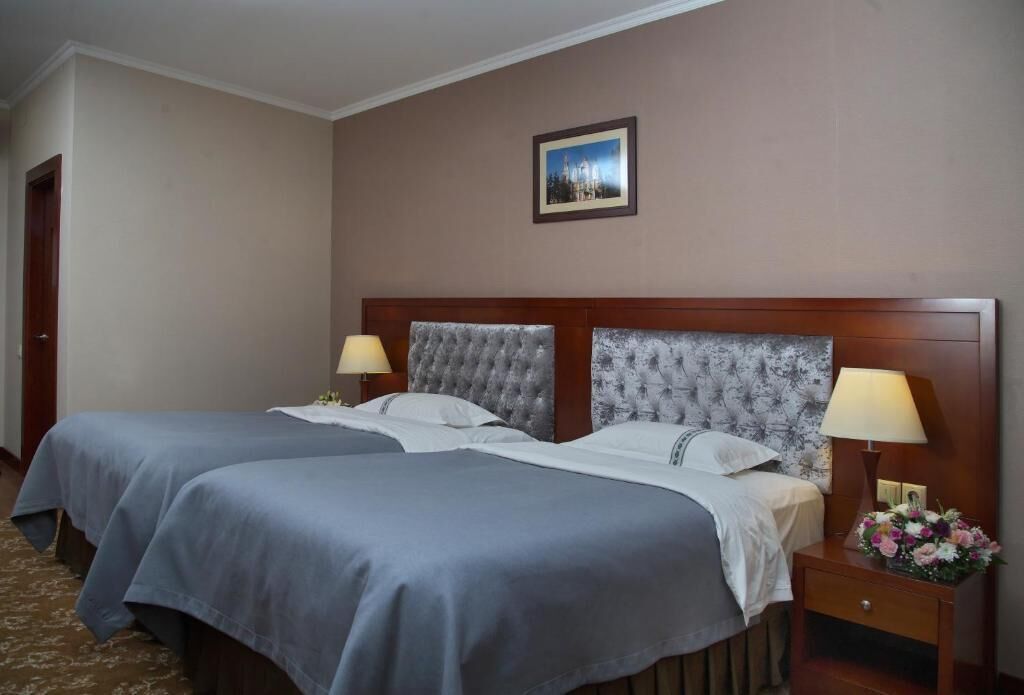 Hotelkamer met twee bedden, een houten hoofdbord, een nachtkastje met lamp en een lijst met een foto aan de muur.