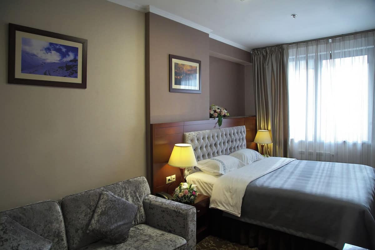 A hotel room with a large bed, two bedside lamps, a headboard, a sofa, and two framed pictures on the wall.