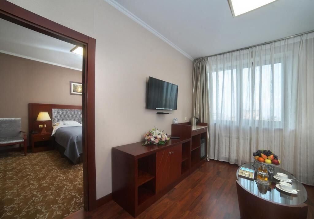 A hotel room with a bed, a TV, a desk with a coffee maker, and a fruit bowl.