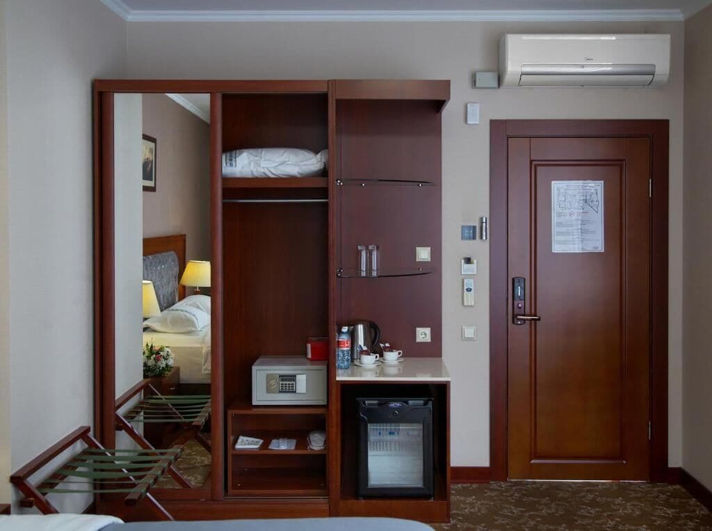 Hotelkamer met een kledingkast, bureau met een magnetron, kleine koelkast, bed en een deur met slot.