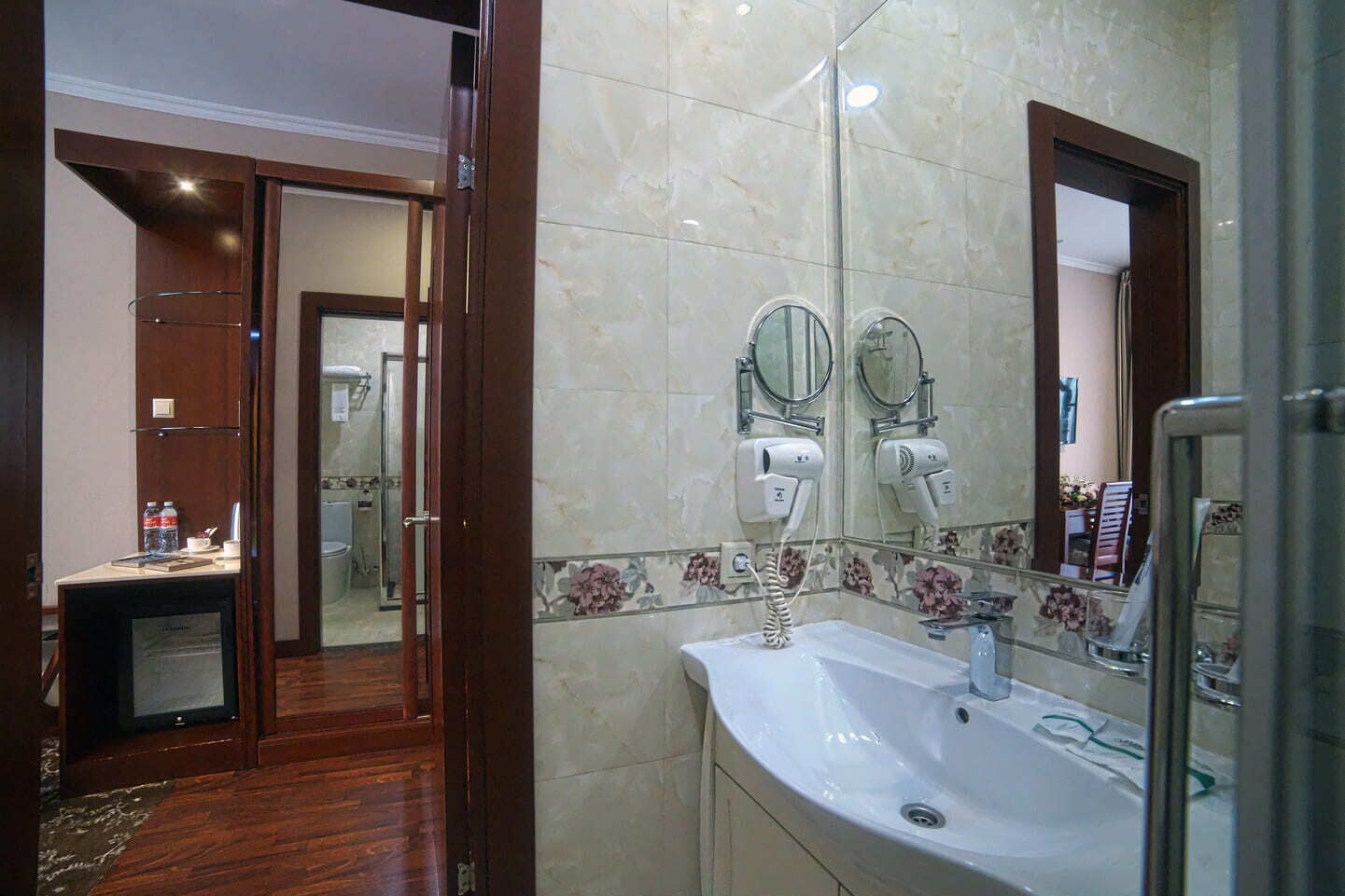 A hotel bathroom with a sink, two mirrors, a hairdryer, and a shower area.