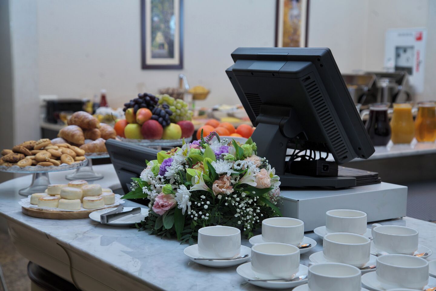 Una mesa de buffet con diferentes platillos, un centro de mesa floral y un monitor de computadora.