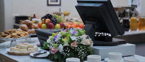 Una mesa de buffet con diferentes platillos, un centro de mesa floral y un monitor de computadora.