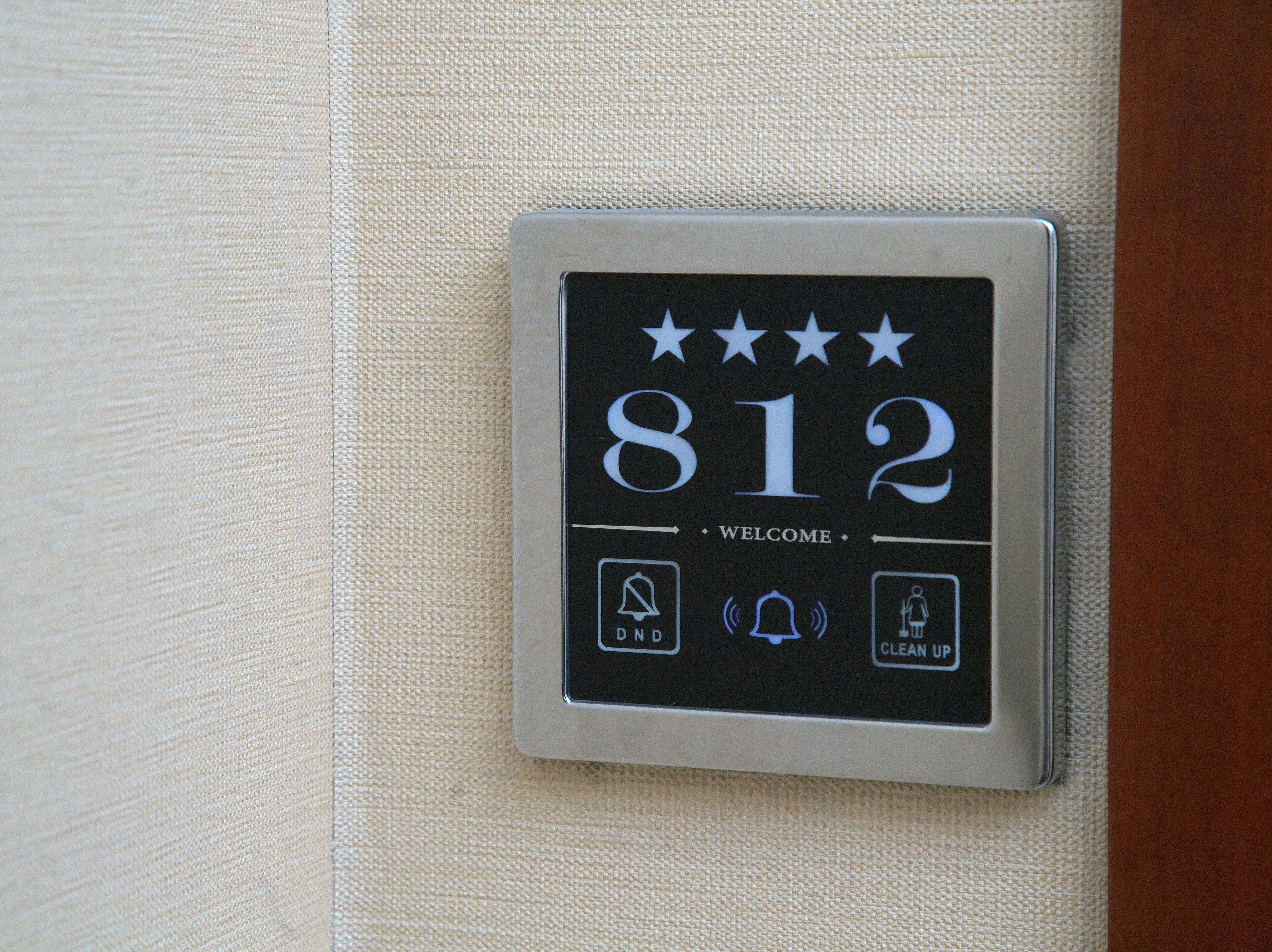 A digital display with the number 812, a welcome message, and icons for a phone, a bell, and a clean-up request.