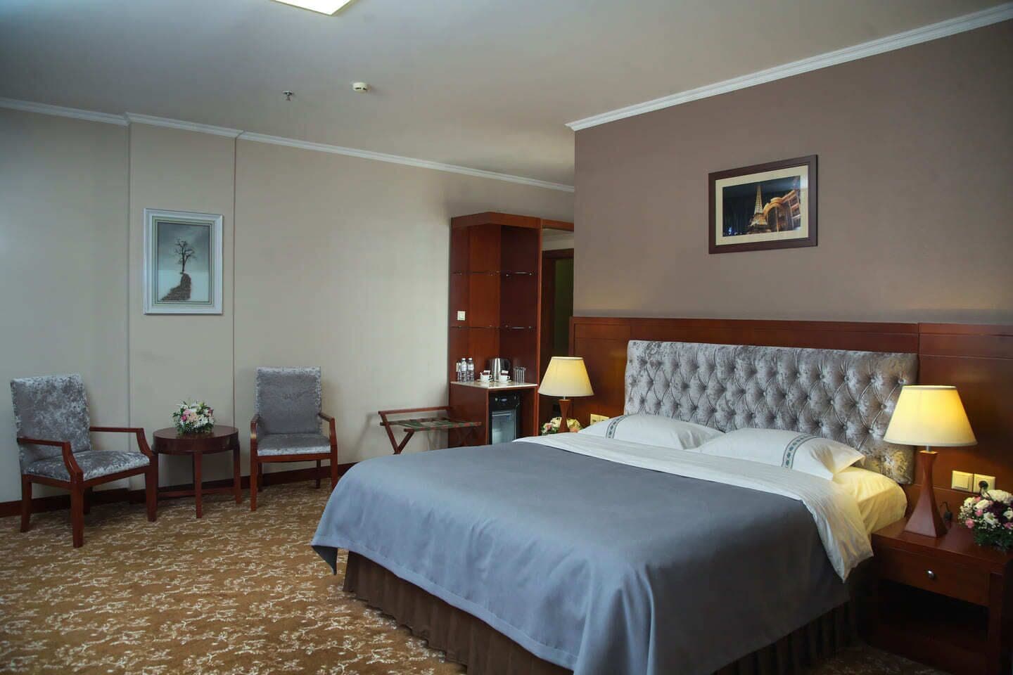A hotel room with a large bed, two chairs, a desk, and a nightstand with lamps.