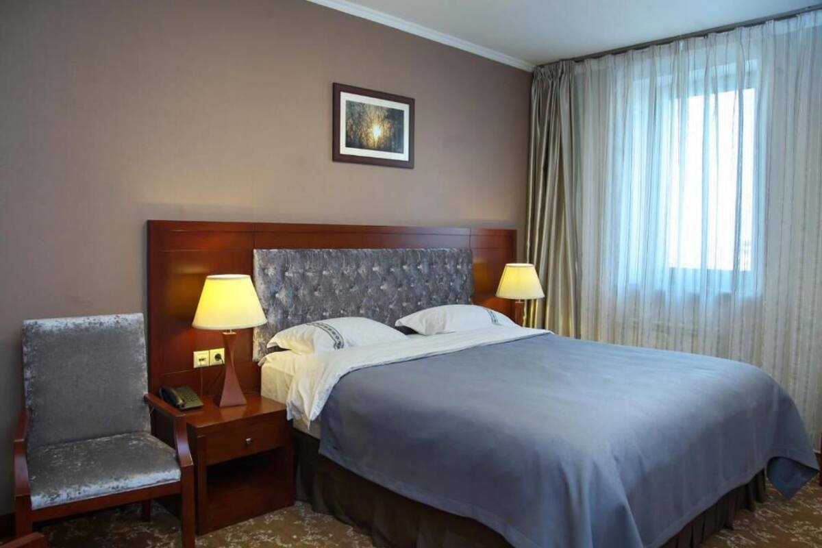 A hotel room with a large bed, two bedside lamps, a chair, a nightstand, and a framed picture on the wall.