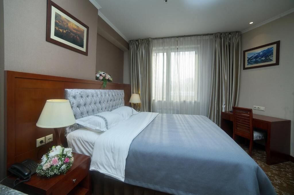 Une chambre d’hôtel avec un grand lit, une tête de lit en bois, un bureau avec une chaise, un téléphone et un vase de fleurs.