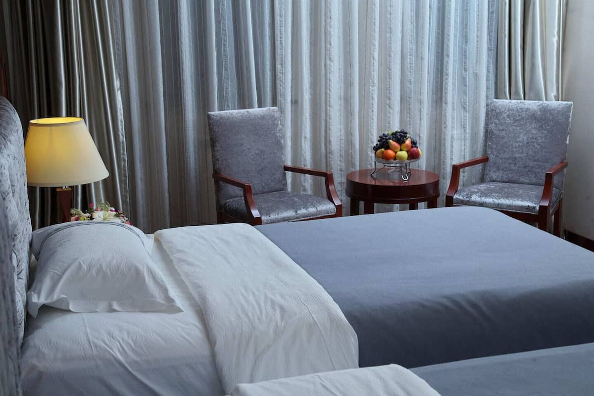 A hotel room with two beds, a round table with fruit, and two armchairs.