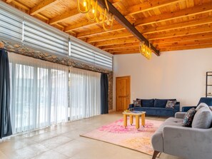 A spacious living room with a wooden ceiling, a large sliding glass door, a blue sofa, and a grey armchair. - Steinhaus in Fethiye Kayaköy by Interhome (Ölüdeniz)