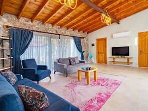 A spacious living room with a stone wall, wooden ceiling, and a TV on a wooden stand. - Steinhaus in Fethiye Kayaköy by Interhome (Ölüdeniz)