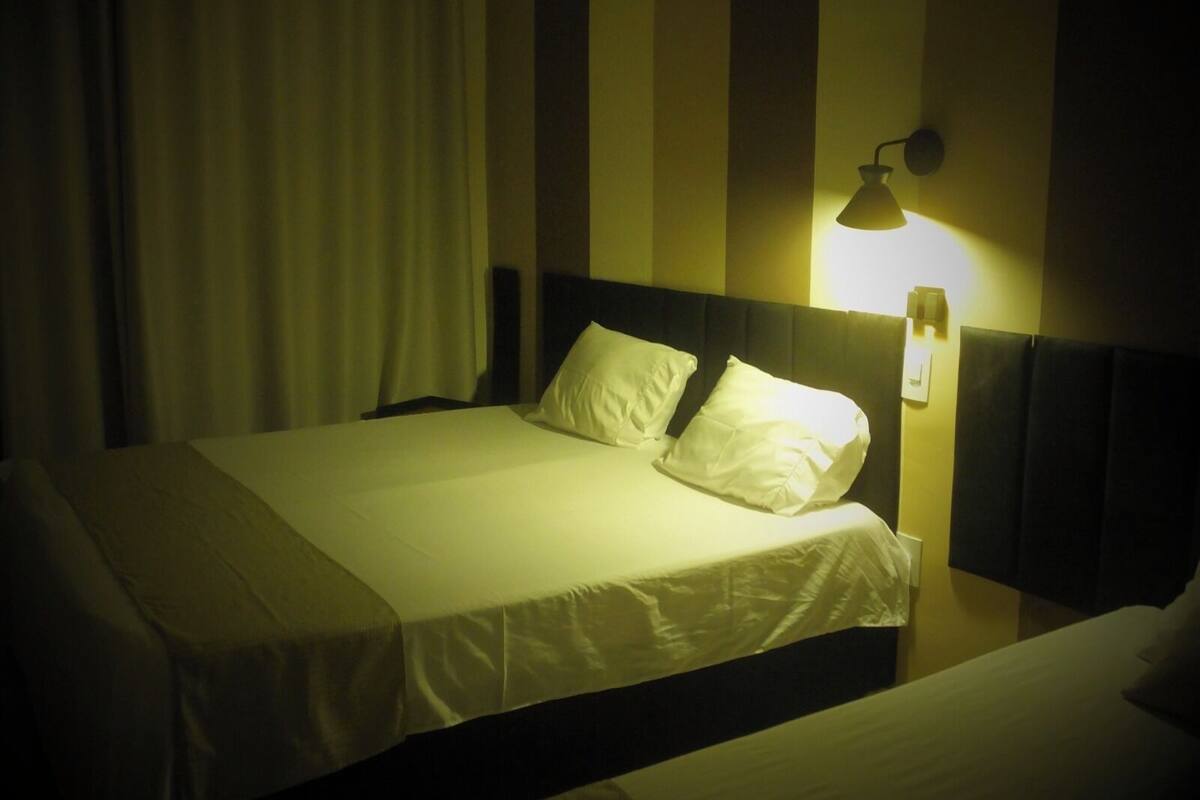 A hotel room with a single bed, a headboard, and a wall-mounted lamp.