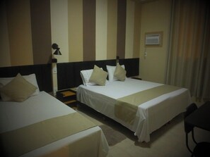 Habitació d'hotel amb dos llits, una tauleta de nit, una làmpada i una finestra amb cortines.