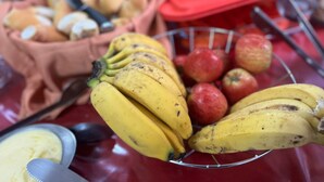 Et bord med en metalklunkebøtte med bananer og æbler, en stofpose med nødder, og en ske.