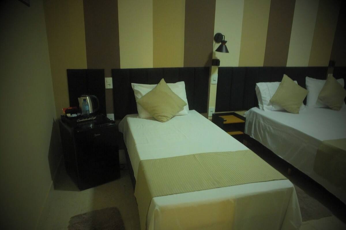 A hotel room with two beds, a nightstand with a lamp, and a small table with a water bottle and a cup.