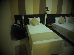 A hotel room with two beds, a nightstand with a lamp, and a small table with a water bottle and a cup.