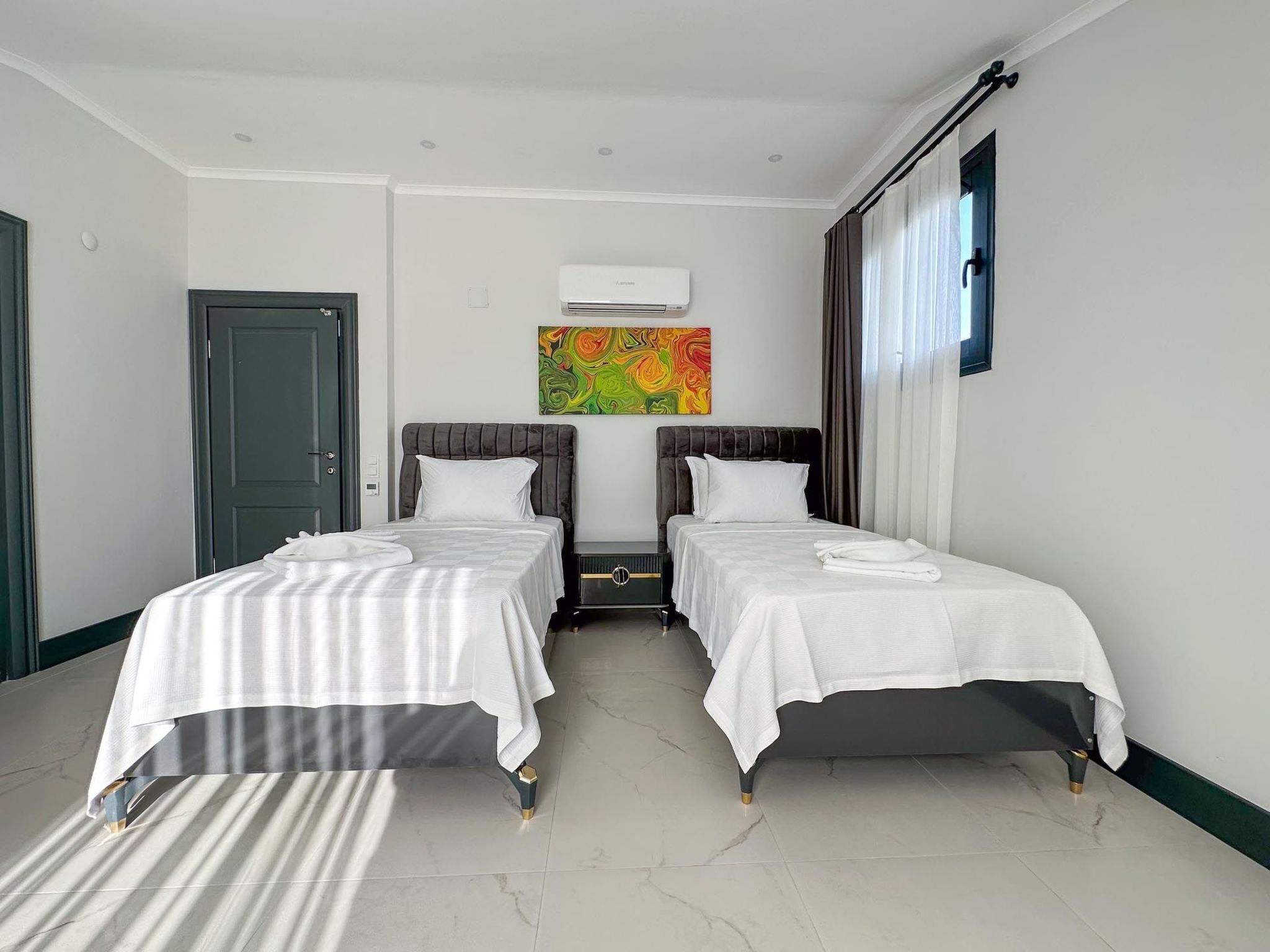 Quarto de hotel com duas camas, um quadro na parede, ar condicionado e janela com cortinas.