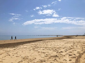 Ein weiter Sandstrand mit Fußspuren und blauem Himmel.
