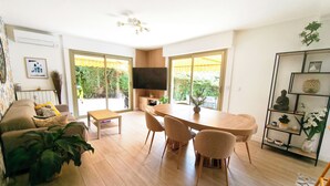 Ein modernes Wohnzimmer mit Sofa, Couchtisch, Esstisch mit Stühlen, Fernseher und Bücherregal.