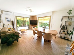 Ein modernes Wohnzimmer mit Sofa, Couchtisch, Esstisch mit Stühlen, Fernseher und Bücherregal.
