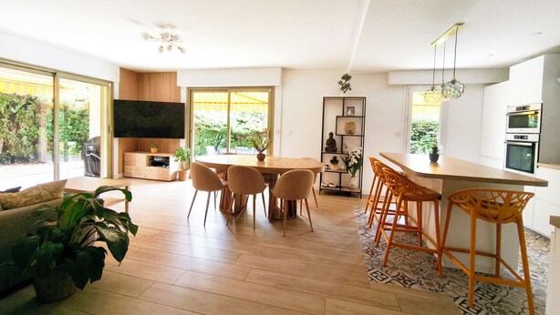 Eine moderne Küche mit einer zentralen Kochinsel, einem Essbereich mit rundem Tisch und Stühlen sowie einem Wohnbereich mit einer Couch und Pflanzen.
