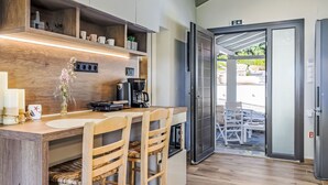 A kitchen with wooden shelves, a coffee machine, and a dining area with chairs. - Villa Pine Trees bei Kardous, Skopelos Privater Pool by Interhome (Skopelos)