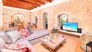 A cozy living room with a stone wall, wooden ceiling beams, a large sofa, a coffee table, and a TV. - "Acrothea Villa Beheizter Pool" by Interhome (Georgioupoli)
