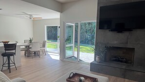 A modern living room with a fireplace, a dining area, and a sliding glass door leading to a backyard. - Private Luxury Oasis – Fully Renovated with Huge Backyard (Mission Viejo)