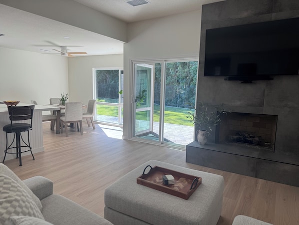 Una sala de estar moderna con chimenea, comedor y puerta corrediza de vidrio que da a un patio trasero.