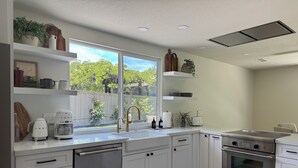 A modern kitchen with white cabinetry, stainless steel appliances, a dishwasher, and a large window overlooking a garden. - Private Luxury Oasis – Fully Renovated with Huge Backyard (Mission Viejo)