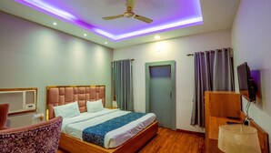 Habitación de hotel con cama, una silla, escritorio, ventilador de techo y televisor.