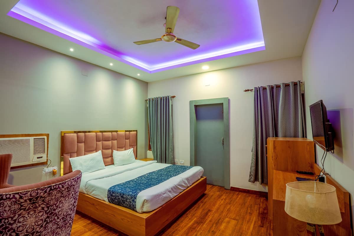 A hotel room with a bed, a chair, a desk, a ceiling fan, and a TV.