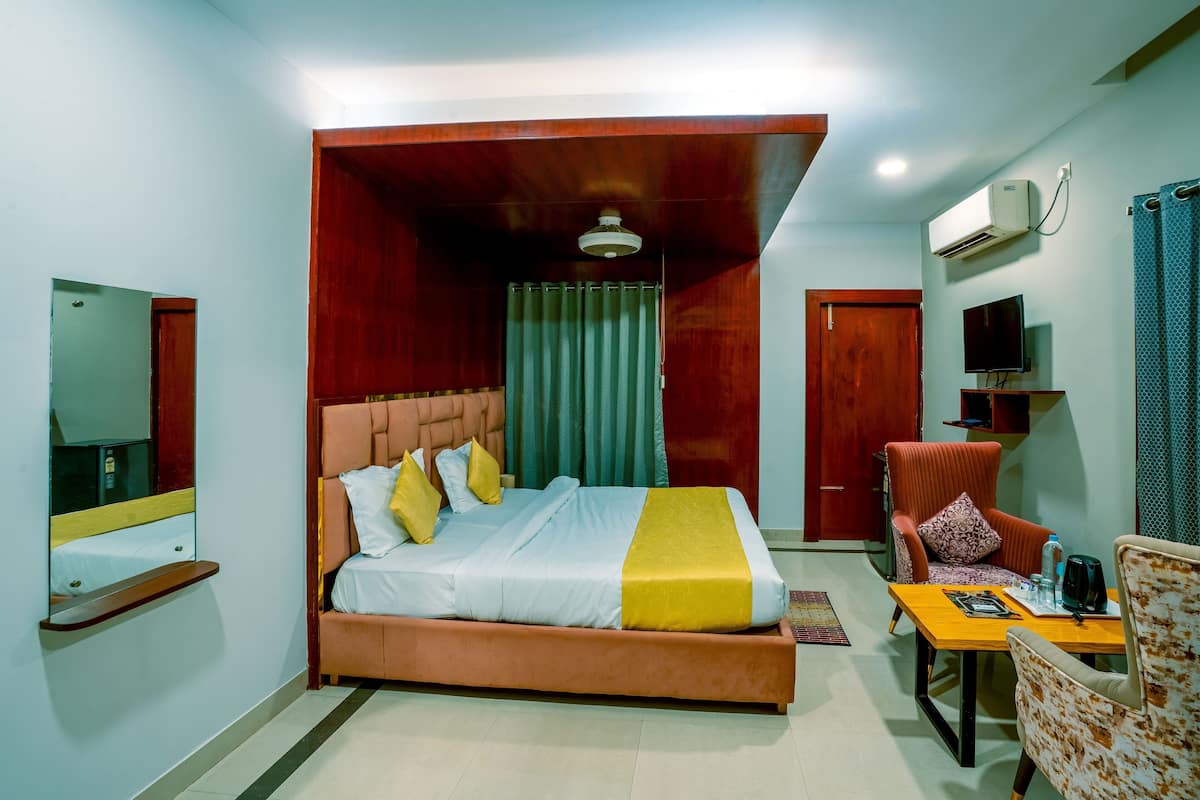 A hotel room with a bed, a chair, a table, a TV, and an air conditioning unit.