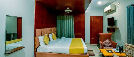 A hotel room with a bed, a chair, a table, a TV, and an air conditioning unit.
