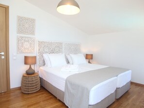 Ein Schlafzimmer mit einem Doppelbett, zwei Nachttischlampen, einem gewebten Beistelltisch und Wanddekoration.