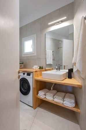 A modern bathroom with a built-in washing machine, a large mirror, and a shelf with folded towels. - Zwei-Zimmer-Wohnung mit atemberaubender Aussicht by Interhome (Kalami)