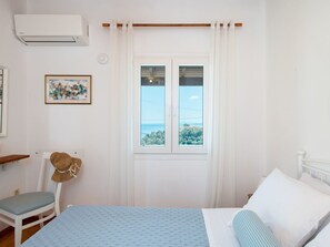 A bedroom with a bed, a chair, a window with curtains, a picture on the wall, and an air conditioning unit. - Zwei-Zimmer-Wohnung mit atemberaubender Aussicht by Interhome (Kalami)