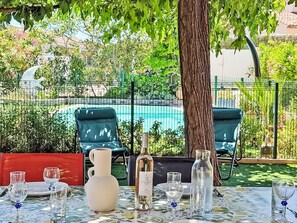 Spiseplads udendørs med en pool i baggrunden, omgivet af grøn vegetation og et hegn.