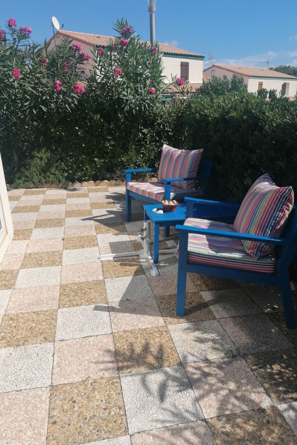 Eine Terrasse mit blauen Gartenmöbeln, einem Schachbrettboden und Blick auf ein Gebäude im Hintergrund.