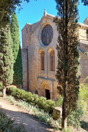 Un edifici de pedra amb una finestra circular gran i portals d'arc, envoltat d'arbres i un camí de terra.