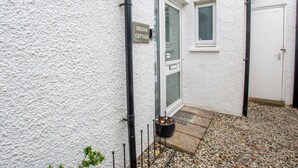 Ein weißes Cottage mit einem Schild, auf dem "Helena Cottage" steht, einer Tür, einem kleinen Fenster, einem schwarzen Metallzaun und einem Kiesweg, der zur Tür führt.