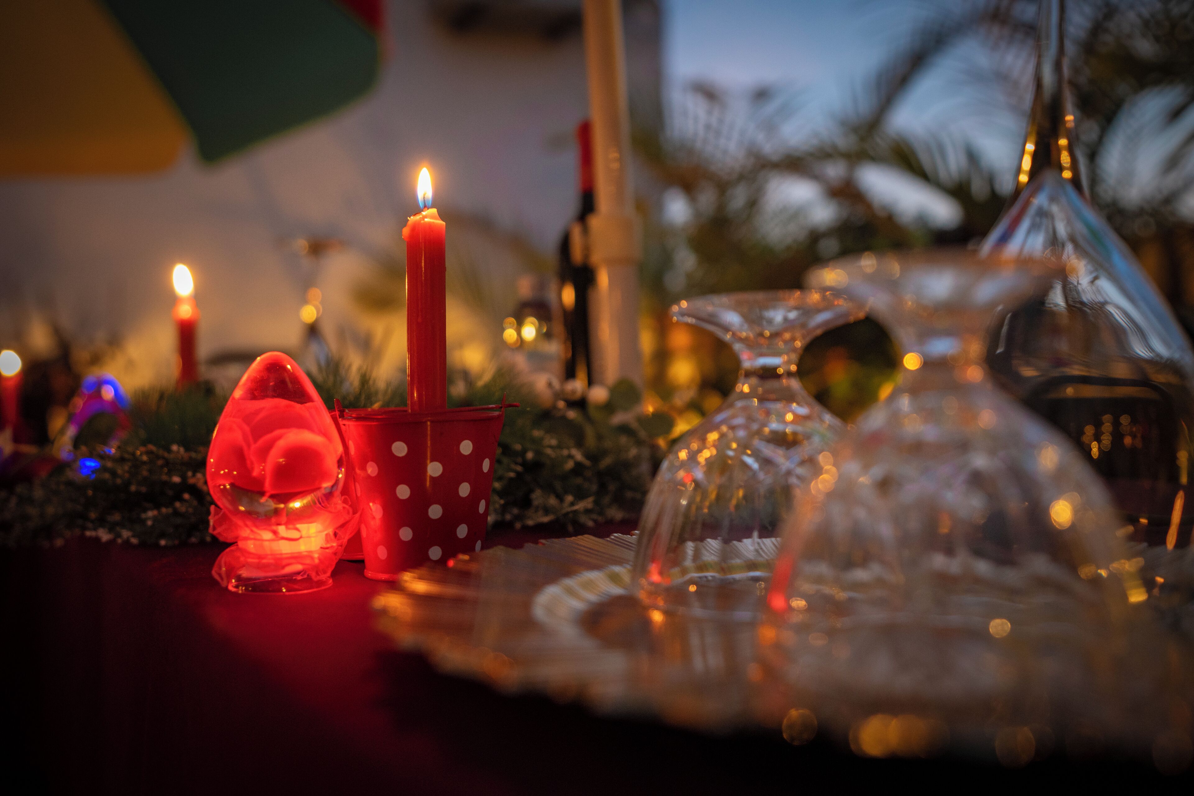 A table with a lit candle, a glass dome, and a red polka-dotted cup.